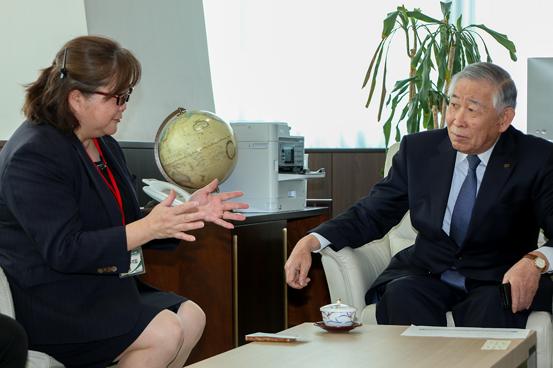 オフィスの応接室で話をしている二人のビジネスパーソン。一人は手を広げながら熱心に話し、もう一人は落ち着いて聞いている