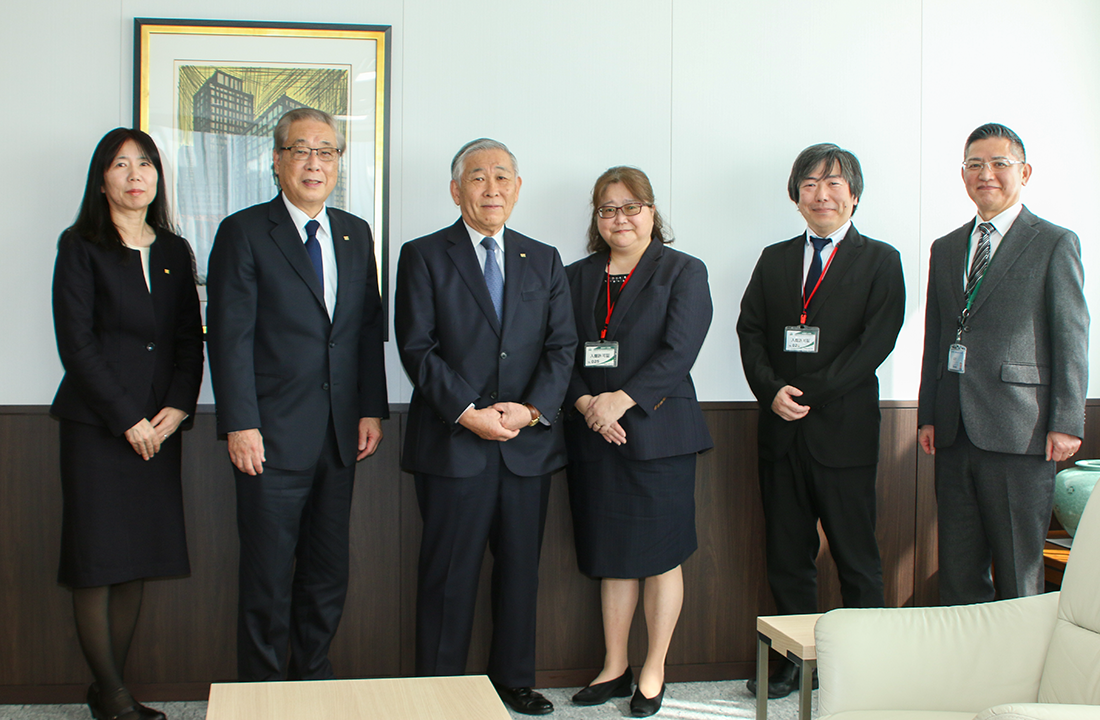 オフィス内で撮影された、フォーマルな服装の6人の集合写真。落ち着いた雰囲気の中、全員がカメラに向かって微笑んでいる