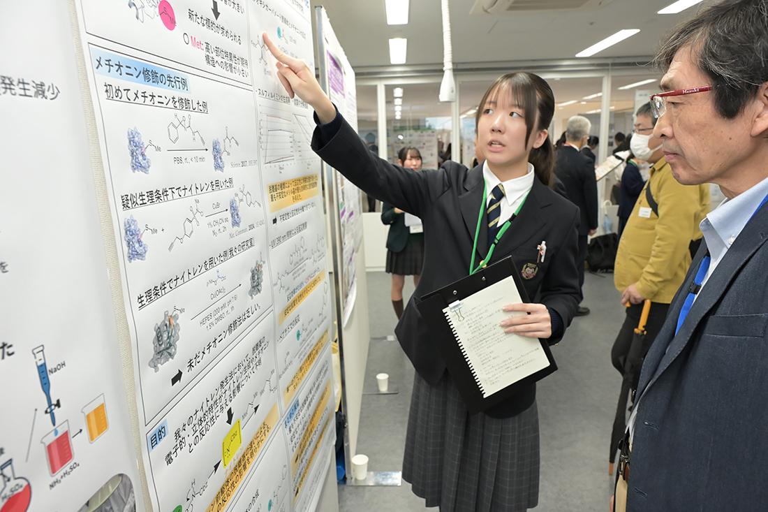 ポスター発表で、生徒が研究ポスターを指さして説明している