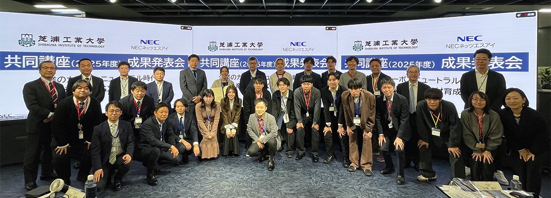 大型スクリーンに共同講座成果発表会の文字が映る会場で、参加者が並ぶ集合写真