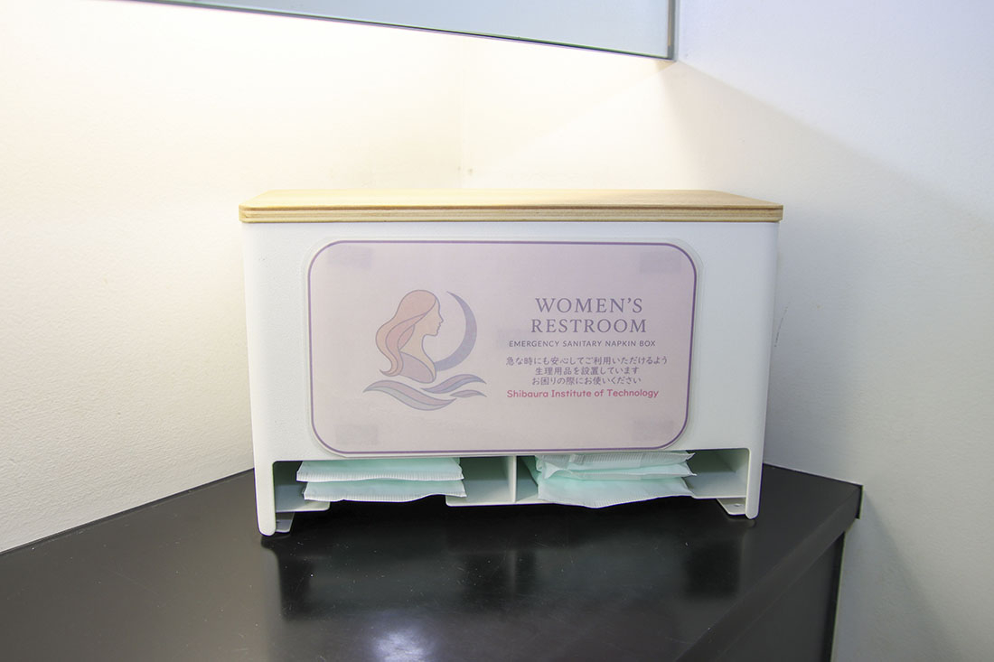 黒い台に置かれた生理用品配布用の装置、ラベルに人魚のイラストあり