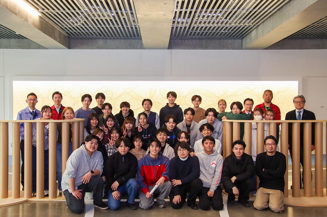 ロビー空間で、約30人のグループが前後2列に分かれて撮影している