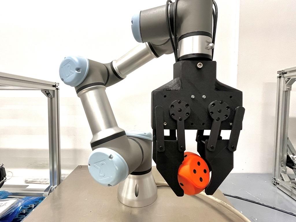 ロボットアームの先端グリッパーが、オレンジ色の部品を保持している